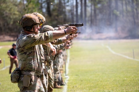 Men in U.S. Army uniforms firing pistols on outdoor pistol range.