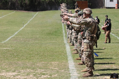 Men in U.S. Army uniforms firing pistols on outdoor pistol range.