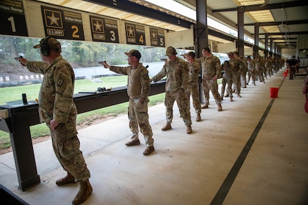 Multiple men in shooting uniforms firing pistol on outdoor pistol range.