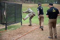 Men in USAMU uniforms instructing U.S. Army Soldier on outdoor firing range.