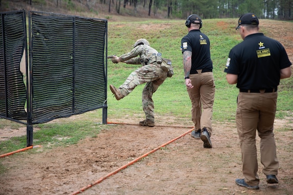 Men in USAMU uniforms instructing U.S. Army Soldier on outdoor firing range.