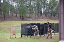 Man in USAMU shooting uniform instructing U.S. Army Soldier on outdoor firing range.