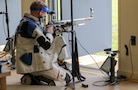 Man in shooting uniform kneeling with air rifle.