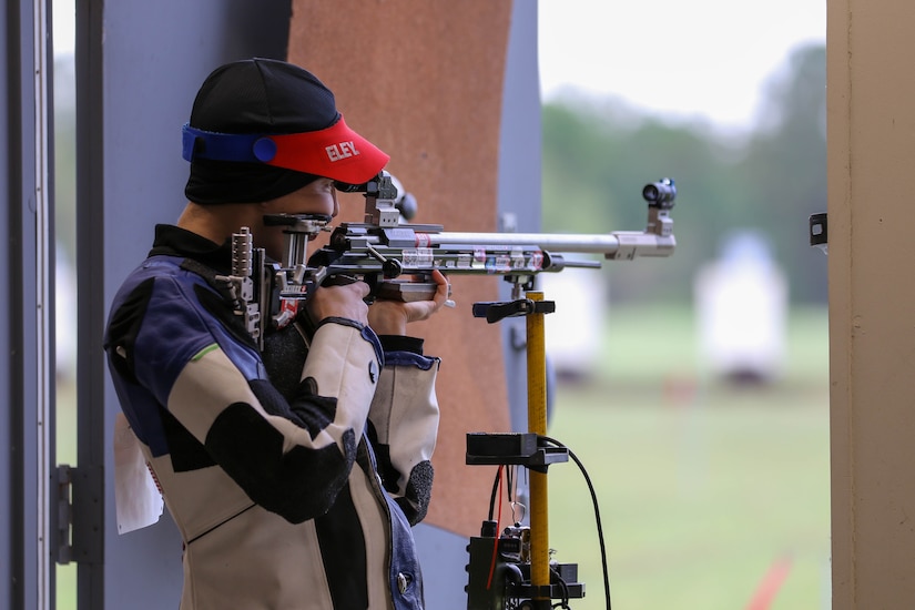 Woman in shooting uniform standing with air rifle.