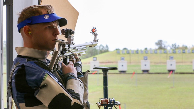 Man in shooting uniform standing with air rifle.