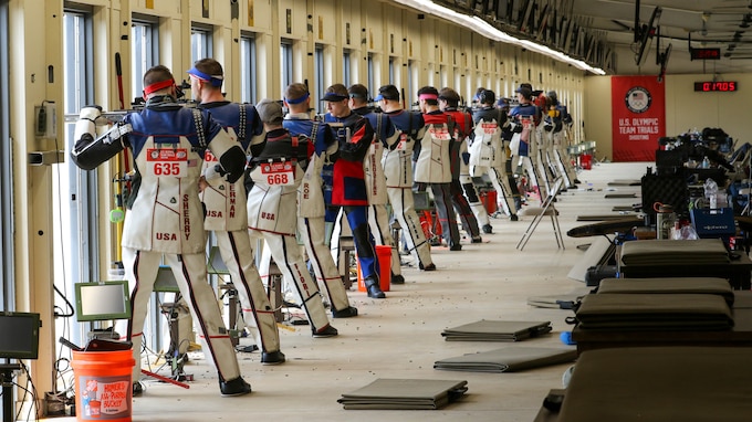 Multiple men in shooting uniforms standing with air rifle.