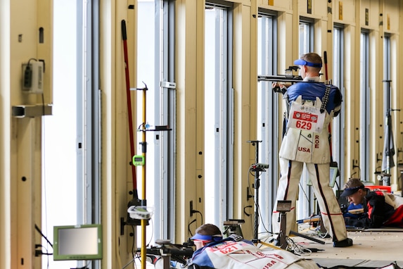 Man in shooting uniform standing with air rifle.