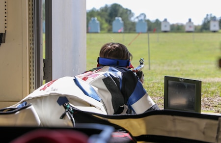 Woman in shooting uniform in prone position with air rifle.