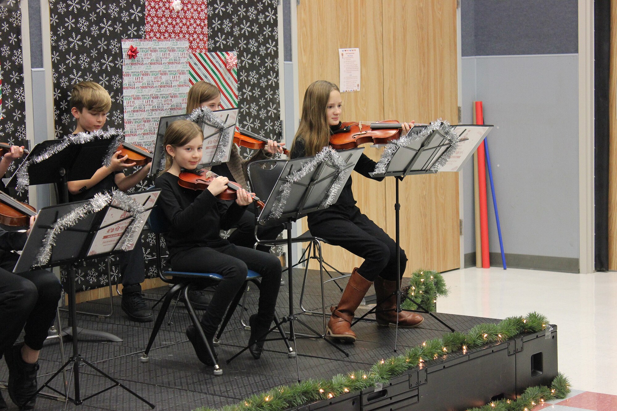A children's orchestra performs songs on violins during a concert.