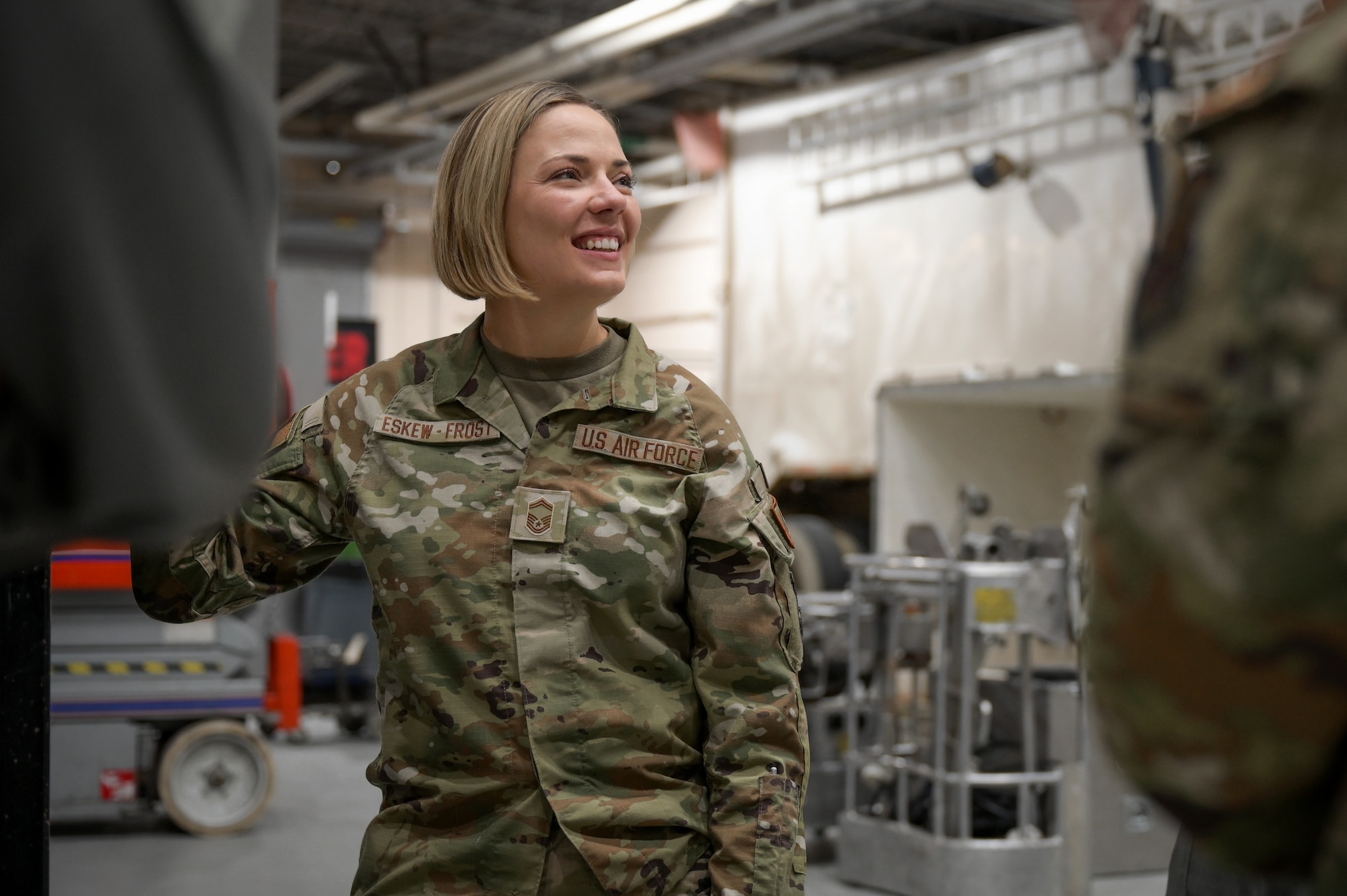 A woman in military uniform and short blonde hair smiles to her right as she speaks with a person out of frame.
