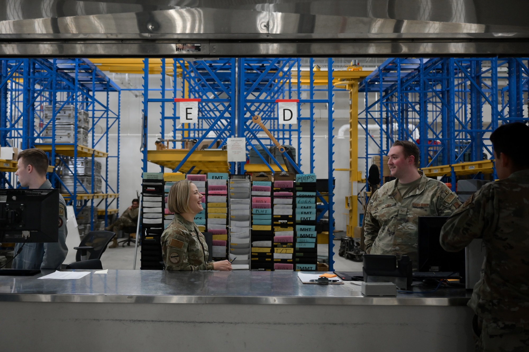 A woman and man in military uniform stand in an equipment bay talking to each other.