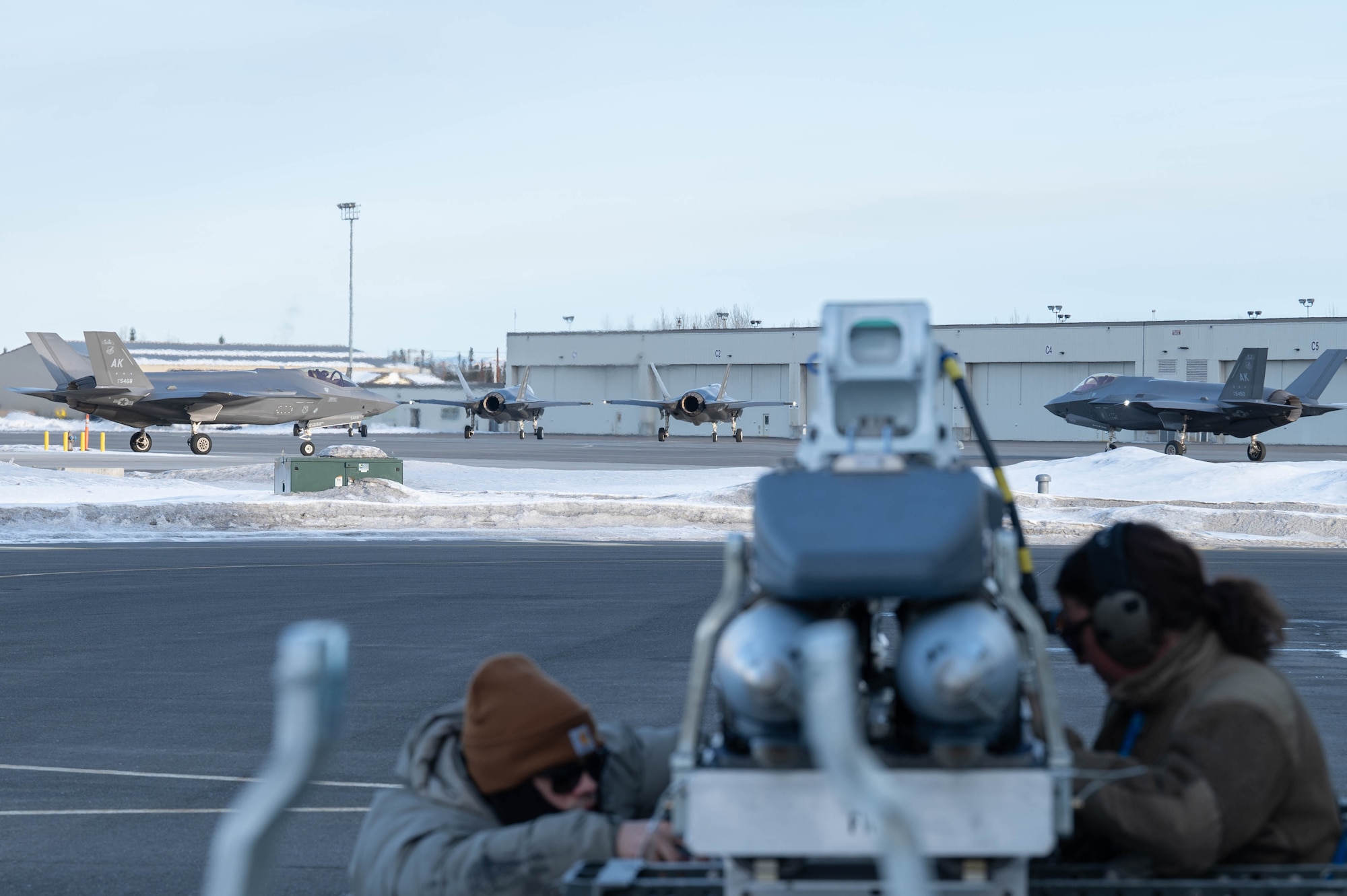 F-35A Lightning II aircraft taxi on the flightline while Airmen assigned to the 355th Fighter Generation Squadron prepare equipment to be loaded during Arctic Gold 24-2 on Eielson Air Force Base, Alaska, March 20, 2024.