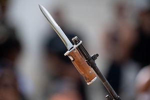 A bayonet (silver knife blade with a brown wooden handle) is affixed to the end of a dark rifle barrel.