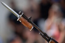 A bayonet (silver knife blade with a brown wooden handle) is affixed to the end of a dark rifle barrel.