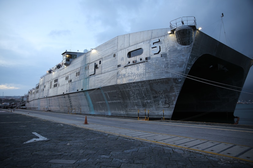 A ship is docked next to a pier with a small orange traffic cone on the dock.