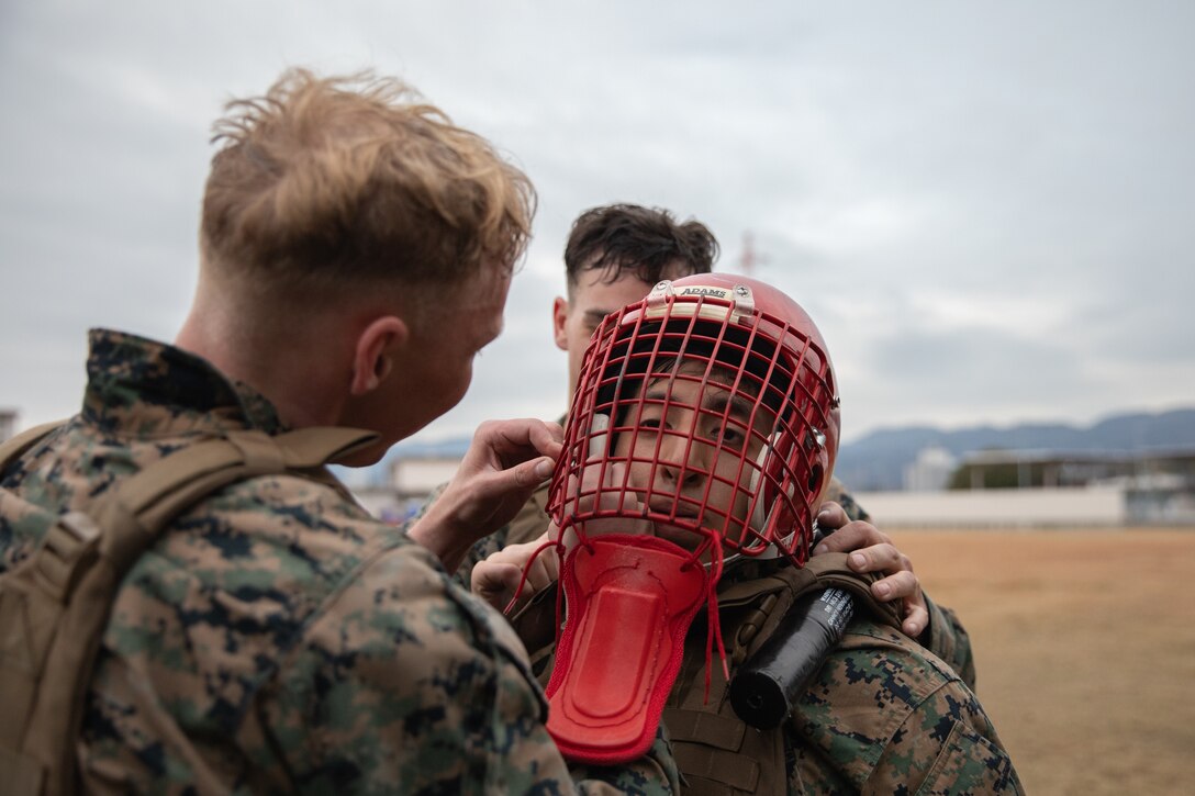 U.S. Marine Corps Sgt. Skylar Madison, a correction and detention specialist with Headquarters and Headquarters Squadron (H&HS), Marine Corps Air Station Iwakuni, left, assists in putting sparring gear on Cpl. Johnathan Culcayveletanga, an air traffic controller with H&HS, MCAS Iwakuni, during the culminating event of a Marine Corps martial arts instructor course at MCAS Iwakuni, Japan, Dec. 14, 2023. Graduates of the 15-day course become qualified Martial Arts Instructors, empowered to independently lead and facilitate courses, assisting lower-belt Marines in their progression towards higher belts. (U.S. Marine Corps photo by Lance Cpl. Colin Thibault)