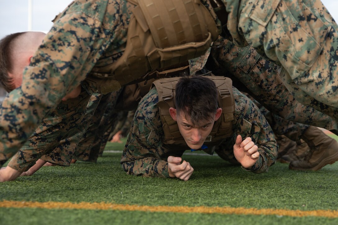 U.S. Marine Corps Cpl. Tre Lessard, a correctional specialist with Headquarters and Headquarters Squadron, Marine Corps Air Station Iwakuni, crawls underneath the Marines in his squad during the culminating event of a Marine Corps martial arts instructor course at MCAS Iwakuni, Japan, Dec. 14, 2023. Graduates of the 15-day course become qualified Martial Arts Instructors, empowered to independently lead and facilitate courses, assisting lower-belt Marines in their progression towards higher belts. (U.S. Marine Corps photo by Lance Cpl. Colin Thibault)