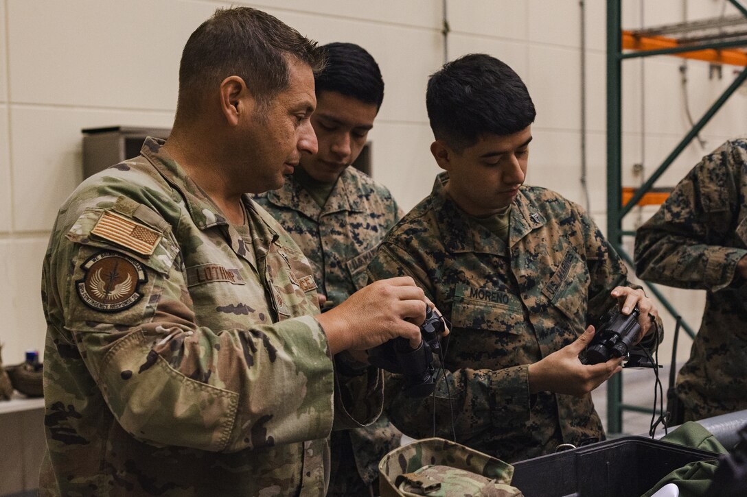 U.S. Air Force Tech. Sgt. Matthew Lothrop, an air transportation specialist with the U.S. Air Force 36th Contingency Response Squadron, 36th Contingency Response Group, left, shows U.S. Marines with the Marine Corps Air Station Iwakuni Distribution Management Office how to operate PVS-14-night vision monocular devices during a training exercise at Marine Corps Air Station Iwakuni, Japan, Dec. 13, 2023.  The U.S. Air Force 36th Contingency Response Group conducted joint training that focused on equipment and process interoperability in a contested logistics environment with the MCAS Iwakuni Headquarters and Headquarters Squadron Logistics Department and members of the Japan Air Self-Defense Force.  (U.S. Marine Corps photo by Cpl. Darien Wright)