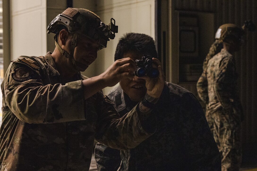 U.S. Air Force Tech. Sgt. Matthew Lothrop, an air transportation specialist with the U.S. Air Force 36th Contingency Response Squadron, 36th Contingency Response Group, left, shows Japan Air Self-Defense Force Capt. Atsushi Kanda, an air traffic controller with Air Traffic Control Group, Air Support Command, how to optimize Gen III AN/AVS-9 night vision goggles during a training exercise at Marine Corps Air Station Iwakuni, Japan, Dec. 13, 2023.  The U.S. Air Force 36th Contingency Response Group conducted joint training that focused on equipment and process interoperability in a contested logistics environment with the MCAS Iwakuni Headquarters and Headquarters Squadron Logistics Department and members of the Japan Air Self-Defense Force.  (U.S. Marine Corps photo by Cpl. Darien Wright)