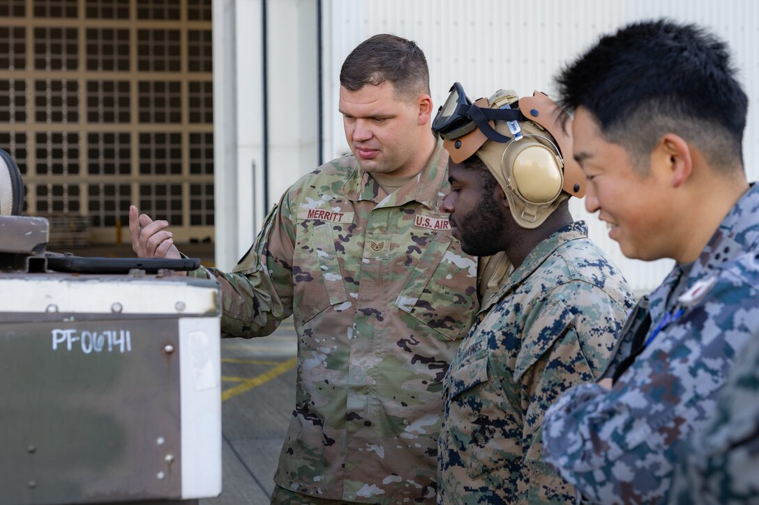 U.S. Air Force Staff Sgt. Ryan Merritt, left, an aerospace ground equipment specialist with the U.S. Air Force 36th Contingency Response Squadron, 36th Contingency Response Group, demonstrates how to operate an A/M32A-60A generator during a training exercise at MCAS Iwakuni, Japan, Dec. 12, 2023. The U.S. Air Force 36th Contingency Response Group conducted joint training that focused on equipment and process interoperability in a contested logistics environment with the MCAS Iwakuni Headquarters and Headquarters Squadron Logistics Department and members of the Japan Air Self-Defense Force.  (U.S. Marine Corps photo by Cpl. Darien Wright)
