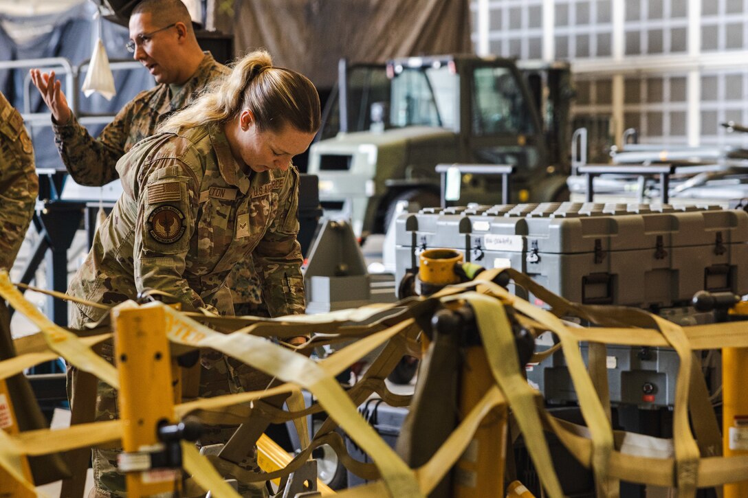 U.S. Air Force Airman 1st Class Abigail Dalton, an air transportation specialist with the U.S. Air Force 36th Contingency Response Squadron, 36th Contingency Response Group, demonstrates how to secure cargo during a training exercise at Marine Corps Air Station Iwakuni, Japan, Dec. 12, 2023. The U.S. Air Force 36th Contingency Response Group conducted joint training that focused on equipment and process interoperability in a contested logistics environment with the MCAS Iwakuni Headquarters and Headquarters Squadron Logistics Department and members of the Japan Air Self-Defense Force.  (U.S. Marine Corps photo by Cpl. Darien Wright)