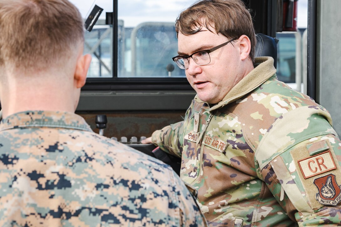 U.S. Air Force Senior Airman Dalton Calhoun, an aerial port journeyman with the U.S. Air Force 36th Contingency Response Squadron, 36th Contingency Response Group, explains how to operate a 25k Halvorsen Next Generation Small Loader during a training exercise at Marine Corps Air Station Iwakuni, Japan, Dec. 12, 2023. The U.S. Air Force 36th Contingency Response Group conducted joint training that focused on equipment and process interoperability in a contested logistics environment with the MCAS Iwakuni Headquarters and Headquarters Squadron Logistics Department and members of the Japan Air Self-Defense Force.  (U.S. Marine Corps photo by Cpl. Darien Wright)