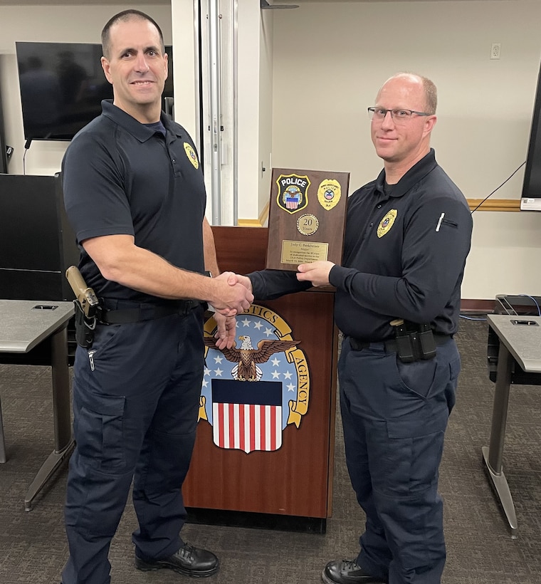 Two police officers shaking hands, one holding a plaque.