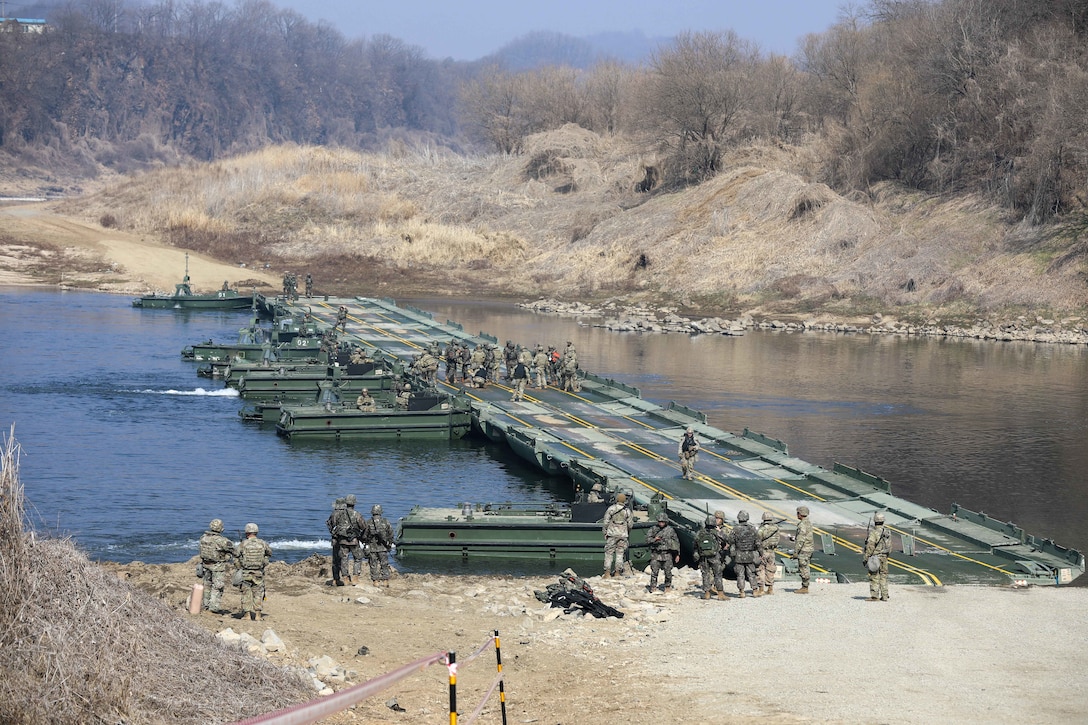 Soldiers build a wide bridge across a river.