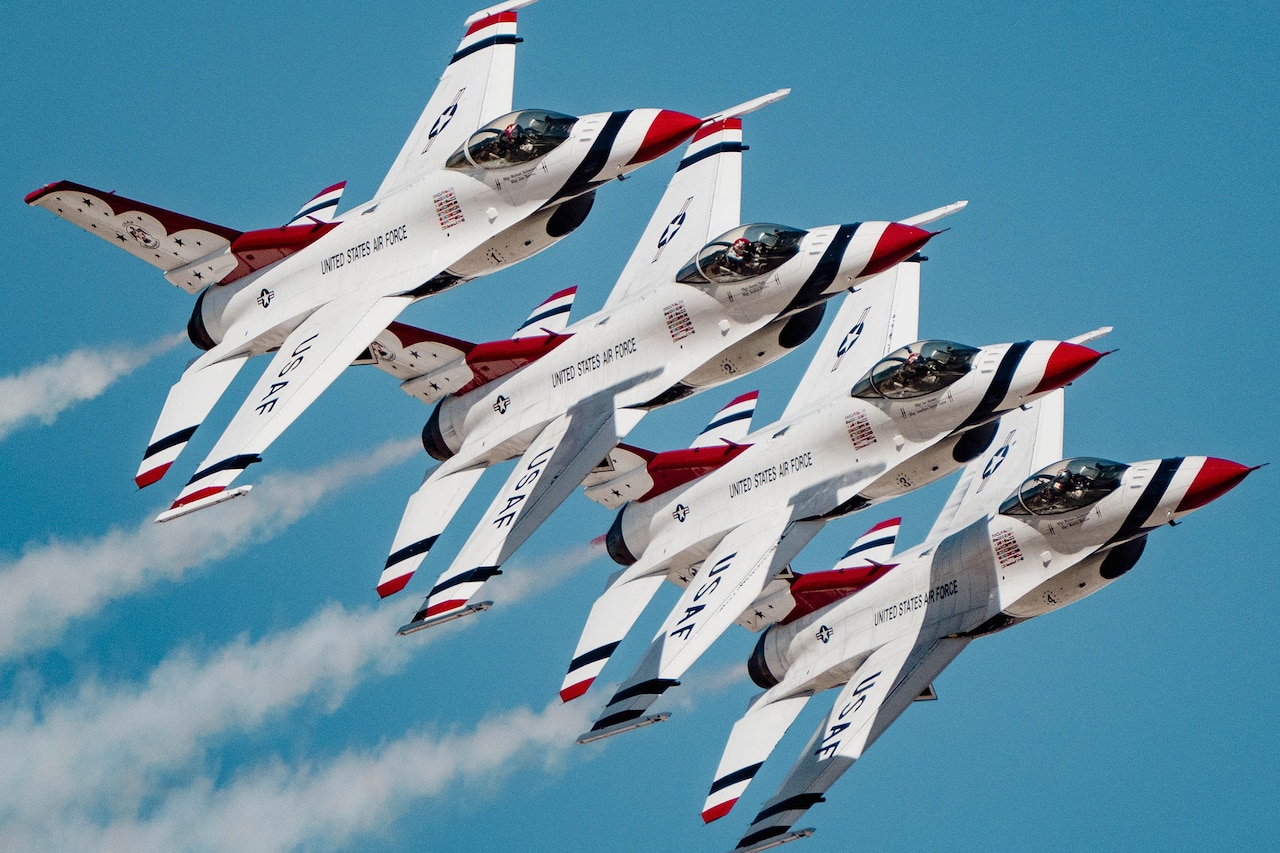 Four military aircraft fly in formation against a bright blue sky.