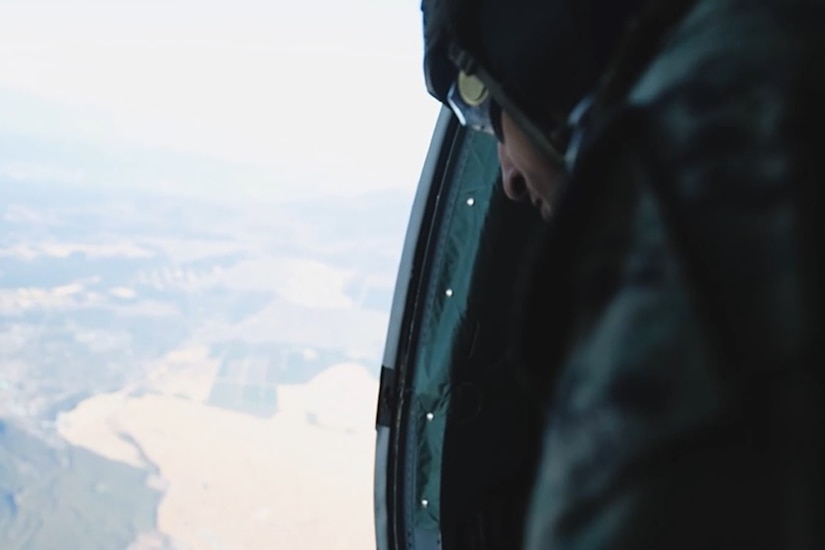 A Marine looks out of an open military aircraft over land.