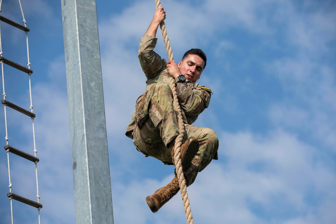 A soldier climbs up a rope next to a ladder under a blue sky.