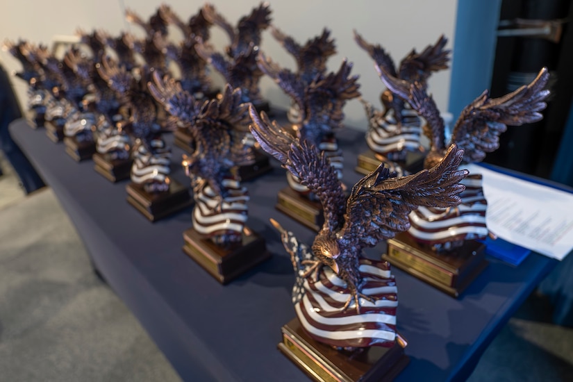 Rows of awards featuring eagles and U.S. flags are lined up on a table.