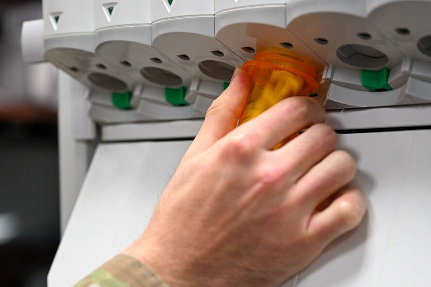 pharmacy technician's hand holds prescription bottle as medication dispenses