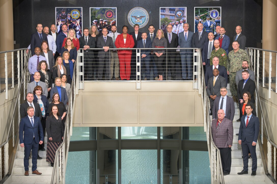 Over two dozen men and women in business attire pose for a photo on a stairwell.