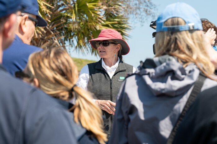 A photo of a woman speaking to a lot of people on a beach.