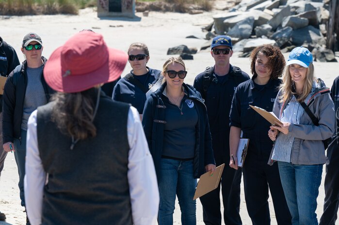 A photo of a woman speaking to a lot of people on a beach.