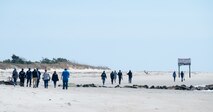 A photo of several people walking down a beach.