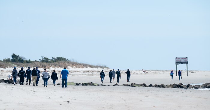 A photo of several people walking down a beach.