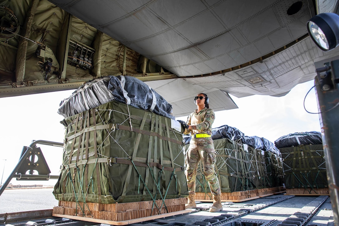 An airman handles cargo on a pallet inside an open aircraft.