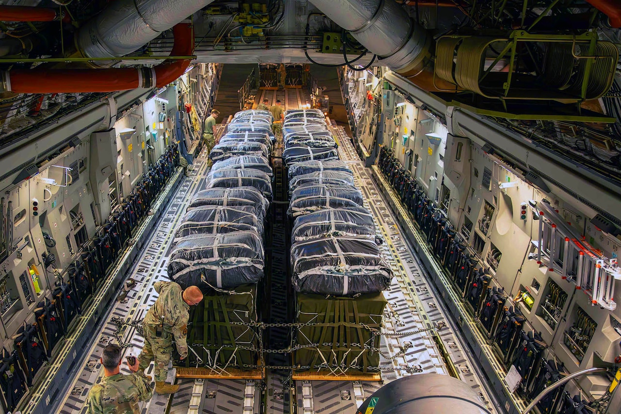 An oblique overhead view of service members handling a large pallet of cargo inside an aircraft.