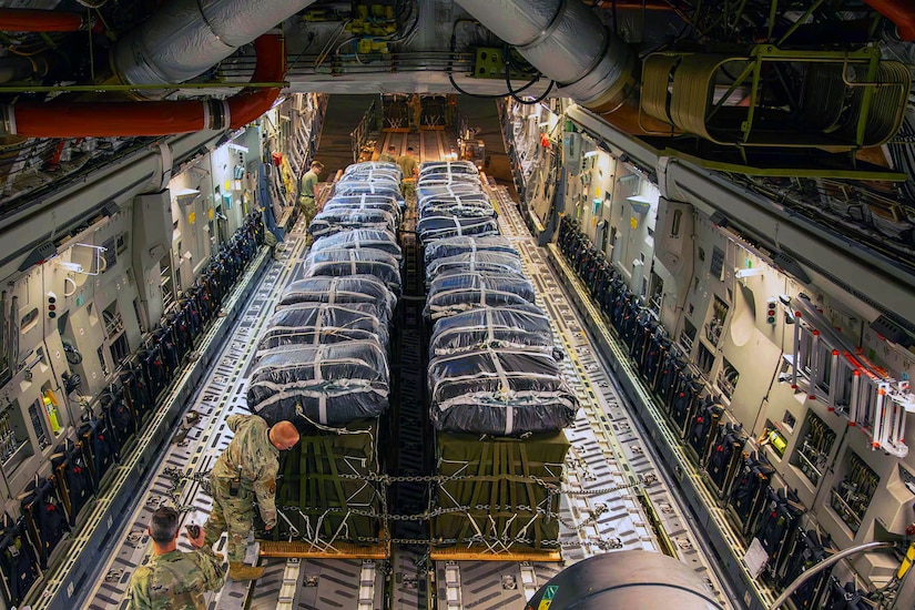 An oblique overhead view of service members handling a large pallet of cargo inside an aircraft.