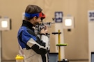 Woman in shooting uniform standing with air rifle.