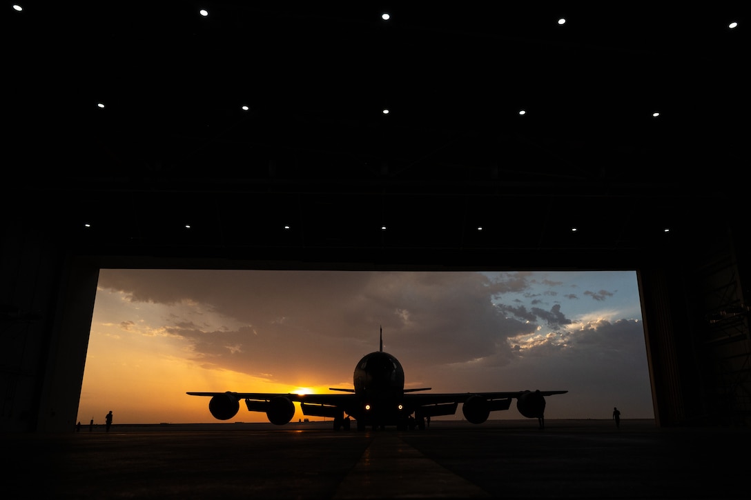 A large aircraft is silhouetted against a twilight sky as it sits outside a hangar.