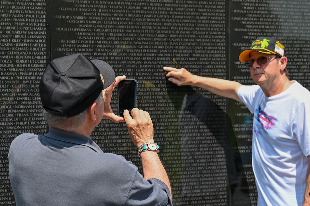 Two people stand next to the Vietnam Veterans Memorial. One takes a picture of the other.