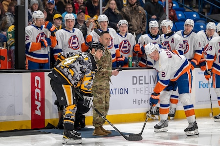A U.S.Army Serviceman stands on the ice rink with a team of hockey players.