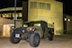 A military vehicle painted in dark camouflage is parked in front of a large arena. The arena's sign reads "Mohegan Sun Arena".