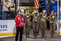 A woman stands at a microphone while singing. Behind her are U.S.Army Servicemembers.