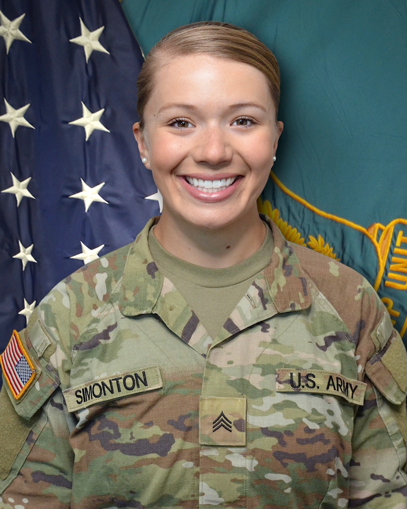 Woman in U.S. Army uniform standing in front of two flags.