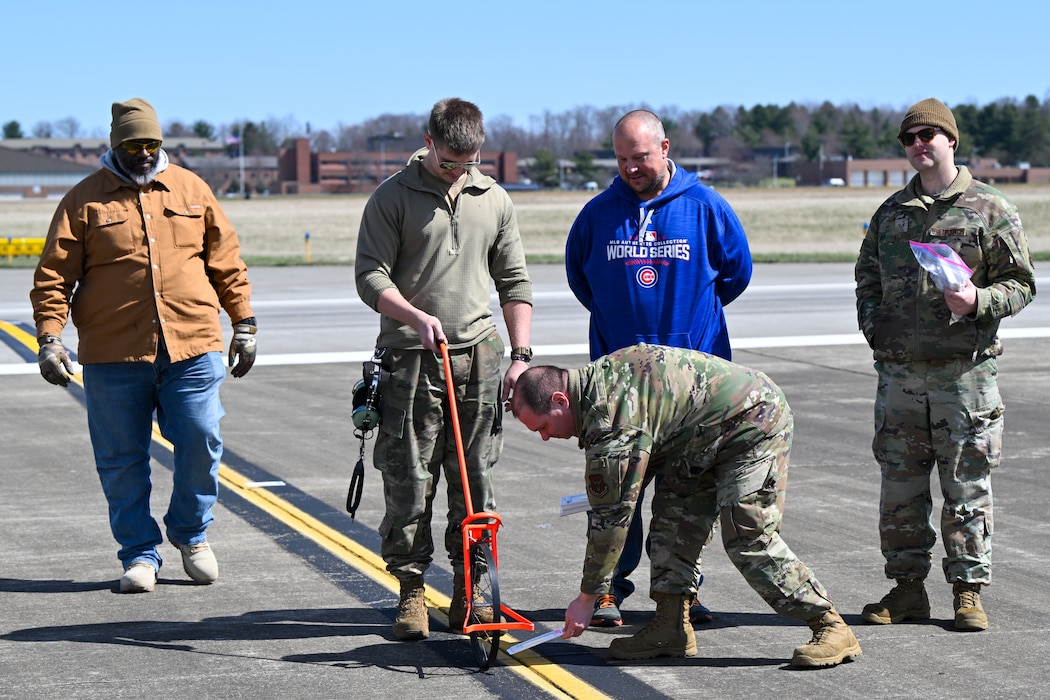 Tech. Sgt. Thomas Wiesen and Senior Airman Dylan Miller, both aerial spray system maintainers assigned to the 910th Maintenance Squadron, place droplet detection cards on the ground in preparation for a water aerial spray test past pass performed by a C-130J-30 Super Hercules aircraft from Keesler Air Force Base, Mississippi, March 25, 2024, at Youngstown Air Reserve Station.