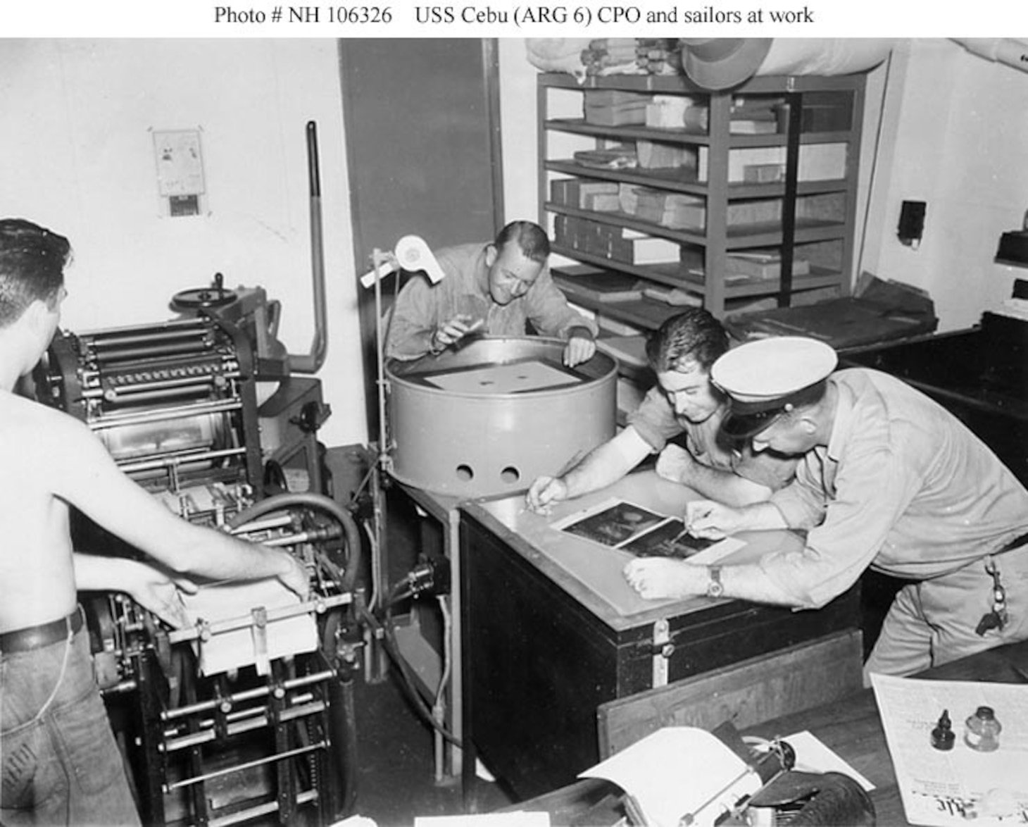 USS Cebu (ARG-6) Sailors and a Chief Petty Officer at work in one of the ship's shops, circa 1944-1945. This appears to be a photo lab, print shop or graphics office. Photograph from the George H. Dunn Album, donated by Charles R. Haberlein Jr., 2008.